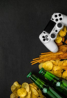 Modern beyaz gamepad cips, kraker ve siyah bir zemin üzerine bira şişesi arasında. Oyun kavramını.