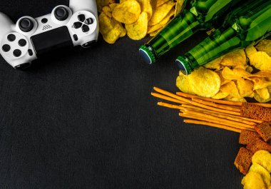 Modern beyaz gamepad cips, kraker ve siyah bir zemin üzerine bira şişesi arasında. Oyun kavramını.