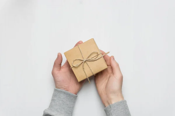 man's hands holds a gift in a box on a white wooden background