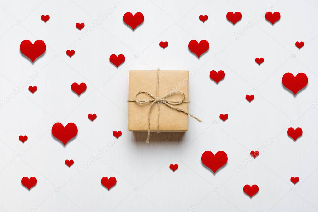 gift box tied with twine surrounded by red hearts on a white wooden background. valentine's day concept