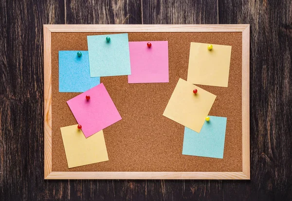 corkboard koyu ahşap zemin üzerine sabitlenmiş çok renkli çıkartmaları ile. Çok renkli boş posta o notlar bir mantar hakları Kurulu.