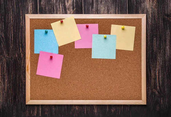 corkboard koyu ahşap zemin üzerine sabitlenmiş çok renkli çıkartmaları ile. Çok renkli boş posta o notlar bir mantar hakları Kurulu.