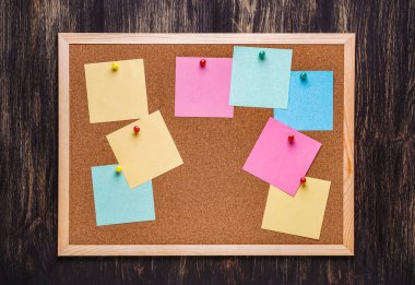 corkboard koyu ahşap zemin üzerine sabitlenmiş çok renkli çıkartmaları ile. Çok renkli boş posta o notlar bir mantar hakları Kurulu.