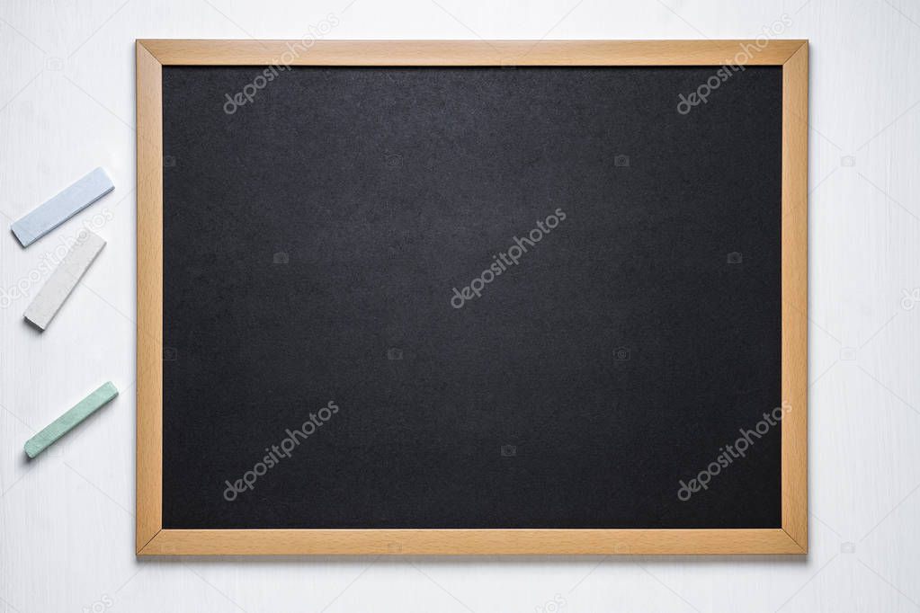 black chalk board and several colored chalk on a white wooden background
