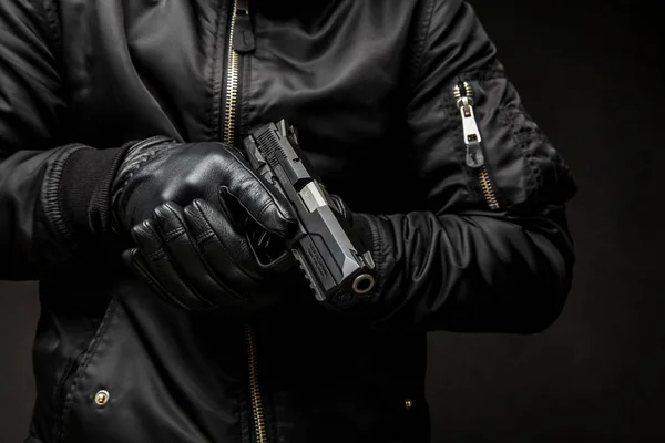 Człowiek w czarną kurtkę i czarne rękawiczki trzyma broń ciemny tyłu — Zdjęcie stockowe
