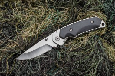 Yeşil dikiş ipliklerinin arka planında katlanır penknife.