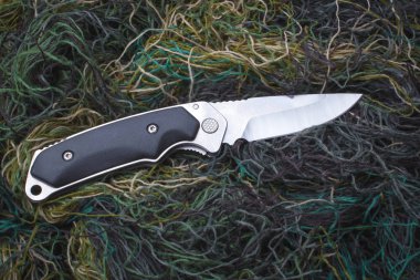 Yeşil dikiş ipliklerinin arka planında katlanır penknife.