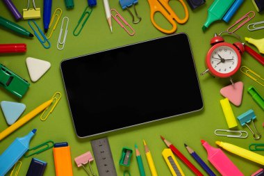Ofis ve okul malzemeleri arasında yeşil bir arka plan üzerinde modern dijital tablet. Okul ofisi malzemeleri kopya alanı olan bir masada. Okul konseptine geri dön.