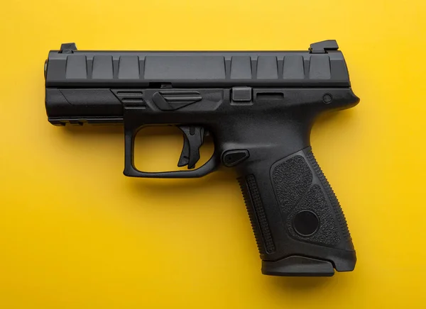 Modern black semi-automatic pistol on a bright yellow background
