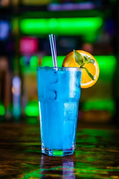 Blue cocktail in a high glass glass with a slice of orange. Colo