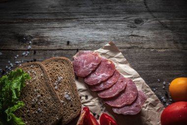 Tahtada dilimlenmiş kurutulmuş et. Sebzeler, ekmek ve et masada. Bir sandviçin bileşenleri.