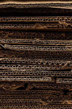 Sıkıştırılmış kıvrımları ve ham kenarları vurgulayan, büyük bir geri dönüştürülmüş karton yığınının desenli yatay yakın çekimi.