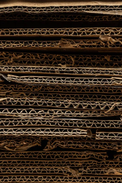 Sıkıştırılmış kıvrımları ve ham kenarları vurgulayan, büyük bir geri dönüştürülmüş karton yığınının desenli yatay yakın çekimi.