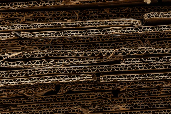 Sıkıştırılmış kıvrımları ve ham kenarları vurgulayan, büyük bir geri dönüştürülmüş karton yığınının desenli yatay yakın çekimi.