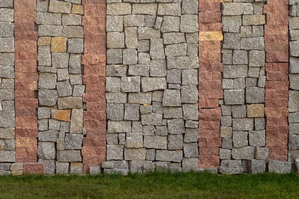 Element der Mauer aus grauen und roten Granitblöcken. in der Nähe des grünen Rasens. — Stockfoto