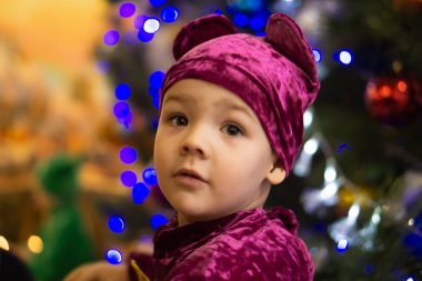 Marmelat ayı. Duygusal çocuk üç yaşında bir yılbaşı ağacı ve mavi fener arka plan üzerinde mor ayı kostümlü