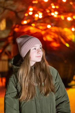 Güzel bir kız gece şehrin parlayan Mağazası fonunda sokak üzerinde aşağı bakıyor. arka plan ile bokeh. Kopya alanı yazıt veya nesneler için.