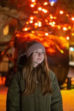 Güzel bir kız gece şehrin parlayan Mağazası fonunda sokak üzerinde aşağı bakıyor. arka plan ile bokeh. Kopya alanı yazıt veya nesneler için