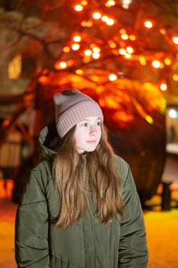 Güzel bir kız gece şehrin parlayan Mağazası fonunda sokak üzerinde aşağı bakıyor. arka plan ile bokeh. Kopya alanı yazıt veya nesneler için