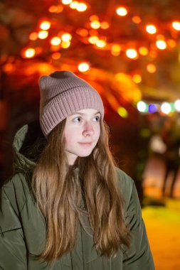 Güzel bir kız gece şehrin parlayan Mağazası fonunda sokak üzerinde aşağı bakıyor. arka plan ile bokeh. Kopya alanı yazıt veya nesneler için