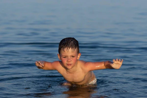 Un niño de tres años está nadando en el mar al atardecer con su hermano . — Foto de Stock