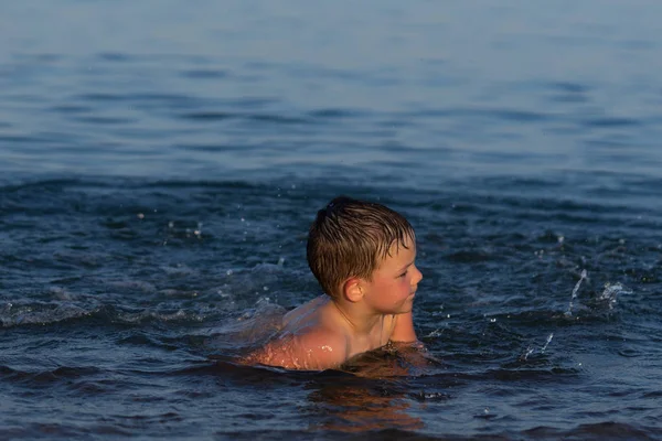 Ein dreijähriger Junge schwimmt mit seinem Bruder bei Sonnenuntergang im Meer. — Stockfoto