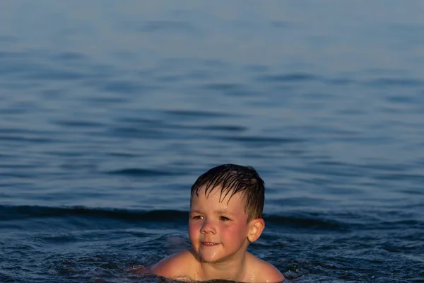 En pojke på tre år simmar i havet vid solnedgången med sin bror. — Stockfoto