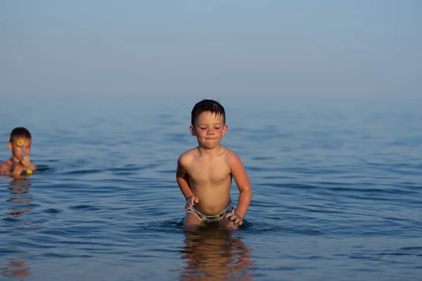 Un niño de tres años está nadando en el mar al atardecer con su hermano . — Foto de Stock