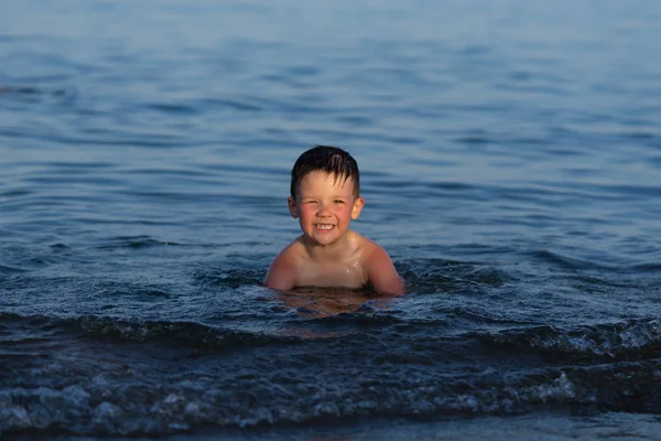 A három éves fiú úszott a tengerben naplementekor a bátyja. — Stock Fotó