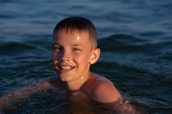 Ein neunjähriger Junge schwimmt bei Sonnenuntergang im Meer. — Stockfoto