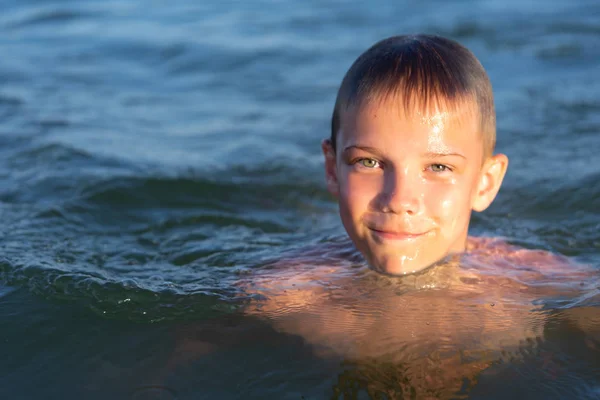 Un ragazzo di nove anni nuota nel mare al tramonto . Foto Stock