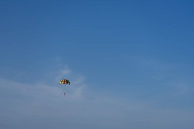 Açık mavi gökyüzüne karşı deniz üzerinde çok renkli bir paraşüt.