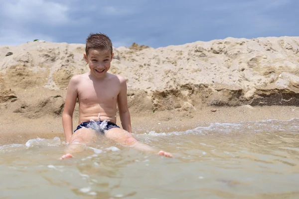Мальчик 9 лет купается и отдыхает на песчаном пляже рядом — стоковое фото