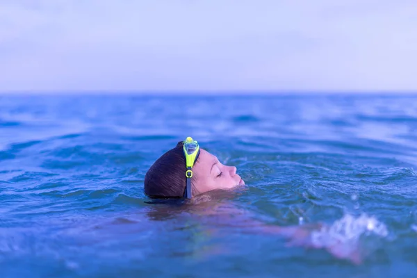 A 10-year-old boy swims in the sea at dawn with glasses for swim — Stock Photo, Image