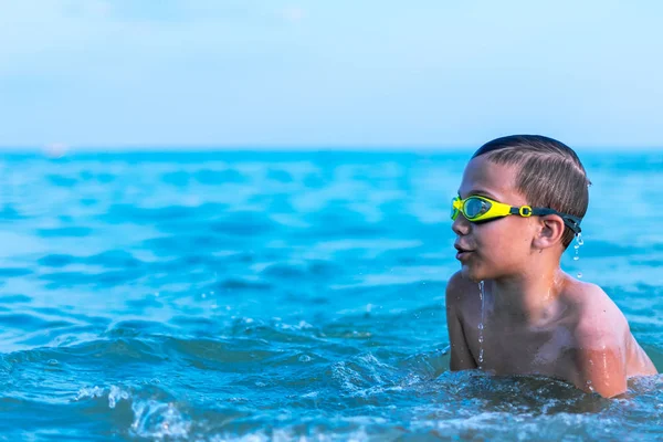 Un niño de 10 años nada en el mar al amanecer con gafas para nadar. — Foto de Stock