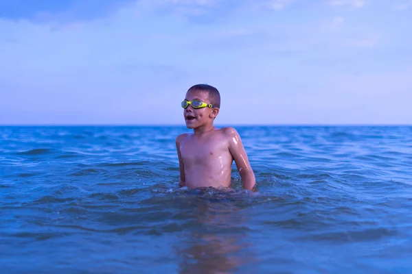 Un niño de 10 años nada en el mar al amanecer con gafas para nadar. — Foto de Stock