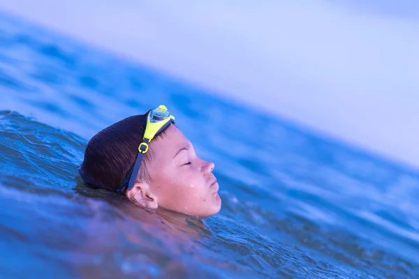 Um menino de 10 anos nada no mar de madrugada com óculos para nadar — Fotografia de Stock
