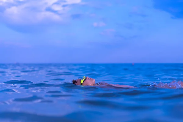 A 10-year-old boy swims in the sea at dawn with glasses for swim