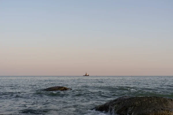 Ένα βαρύ πλοίο με φορτίο εισέρχεται στο λιμάνι με το ρυμουλκό. Στο λιμάνι του Γιούννι. Παράκτιες πέτρες στο προσκήνιο. Επιλεκτική εστίαση. 2019.09.01. Ουκρανία. — Φωτογραφία Αρχείου