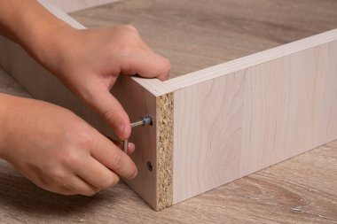 Ahşap yonga mobilyalarını monte eden bir zanaatkarın elleri. Sıkıştırılıyor Vida