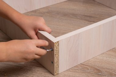 Ahşap yonga mobilyalarını monte eden bir zanaatkarın elleri. Sıkıştırılıyor Vida