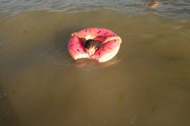 Neşeli bir çocuk güneşli bir günde şişme bir yüzükle denizde yüzer.