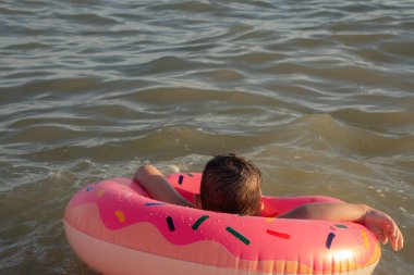 Neşeli bir çocuk güneşli bir günde şişme bir yüzükle denizde yüzer.
