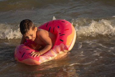 Neşeli bir çocuk güneşli bir günde şişme bir yüzükle denizde yüzer.