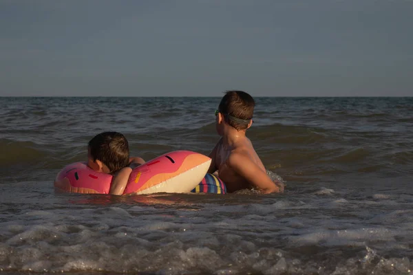 一个5岁的男孩和他10岁的哥哥在海里游泳 带着一个甜甜圈形状的充气圈 两个兄弟沉溺在水里 — 图库照片