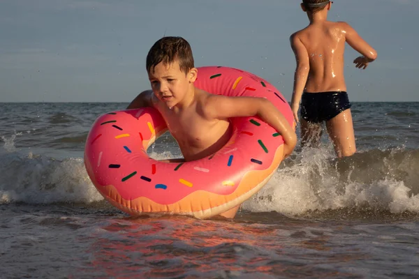 5 yaşındaki bir çocuk 10 yaşındaki abisiyle donut şeklinde şişirilebilir bir çemberle denizde yüzüyor. İki kardeş suya dalar.