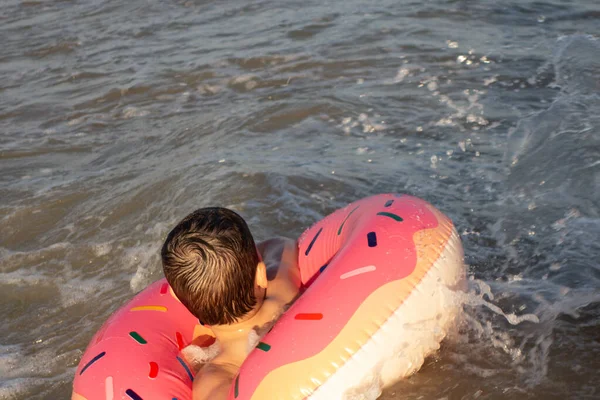 A cheerful boy 5 years old swims in the sea on an inflatable ring in the form of a donut on a sunny day