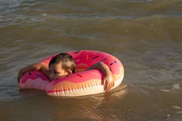 A cheerful boy 5 years old swims in the sea on an inflatable ring in the form of a donut on a sunny day