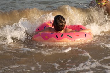 Neşeli bir çocuk güneşli bir günde şişme bir yüzükle denizde yüzer.