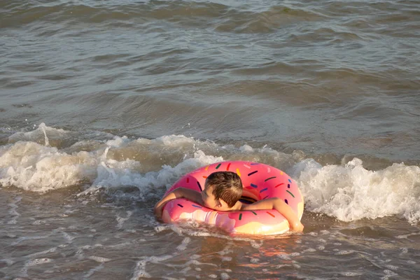 在阳光灿烂的日子里 一个快乐的5岁男孩在一个充气的圆环上 以甜甜圈的形式在海里游泳 — 图库照片